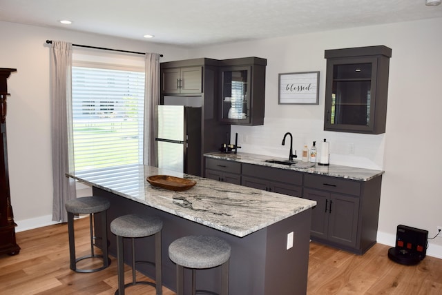 5445 Kestrel Pkwy, Omaha, NE 68022 - kitchen with freestanding refrigerator, a kitchen bar, light stone counters, light wood finished floors, and recessed lighting