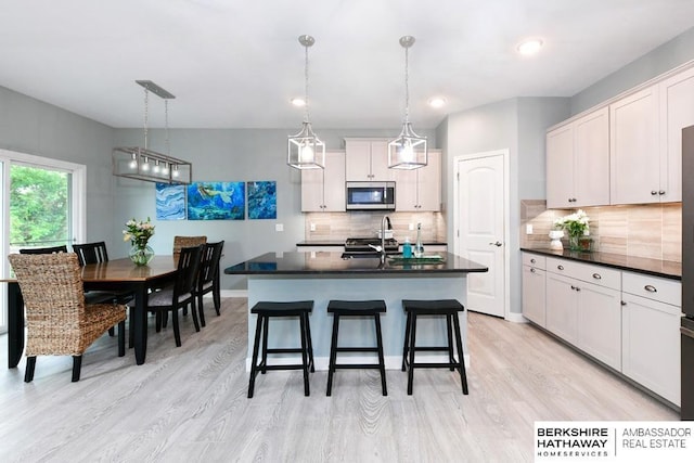 10818 S 109th St, Papillion, NE 68046 - kitchen featuring stainless steel microwave, dark countertops, backsplash, a breakfast bar area, and light wood finished floors