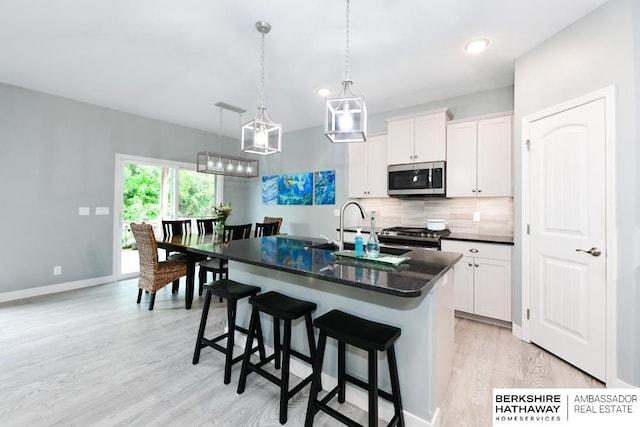 10818 S 109th St, Papillion, NE 68046 - kitchen featuring appliances with stainless steel finishes, light wood-type flooring, backsplash, an island with sink, and white cabinetry
