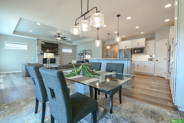 5017 N 209th St, Elkhorn, NE 68022 - dining area featuring light wood finished floors, a ceiling fan, recessed lighting, a stone fireplace, and a tray ceiling