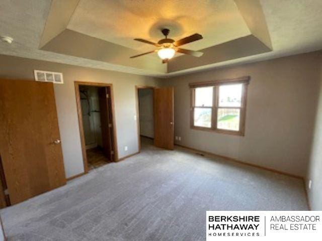 220 Orchard Pl, Hickman, NE 68372 - unfurnished bedroom featuring a raised ceiling, ensuite bathroom, light colored carpet, a spacious closet, and a ceiling fan