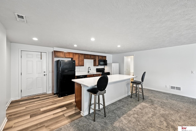 20459 C St, Omaha, NE 68022 - kitchen featuring black appliances, a kitchen bar, recessed lighting, light countertops, and a textured ceiling