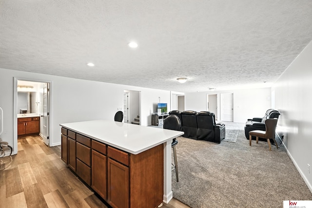 20459 C St, Omaha, NE 68022 - kitchen featuring a center island, light countertops, a textured ceiling, brown cabinetry, and light wood-style flooring