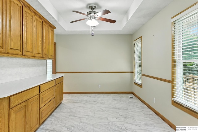 1422 N 155th Ave, Omaha, NE 68154 - kitchen featuring light marble finish flooring, brown cabinets, a ceiling fan, backsplash, and a raised ceiling