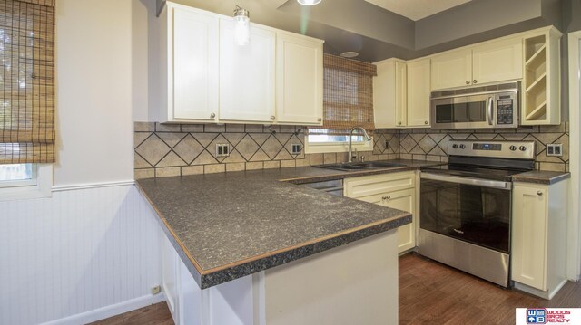 4211 S 36th St, Lincoln, NE 68506 - kitchen with stainless steel appliances, dark countertops, dark wood-style floors, a peninsula, and a wainscoted wall