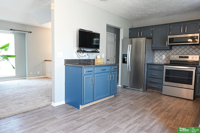 2412 Lewis And Clark Rd, Bellevue, NE 68123 - kitchen featuring appliances with stainless steel finishes, blue cabinetry, decorative backsplash, light wood-style flooring, and dark stone counters
