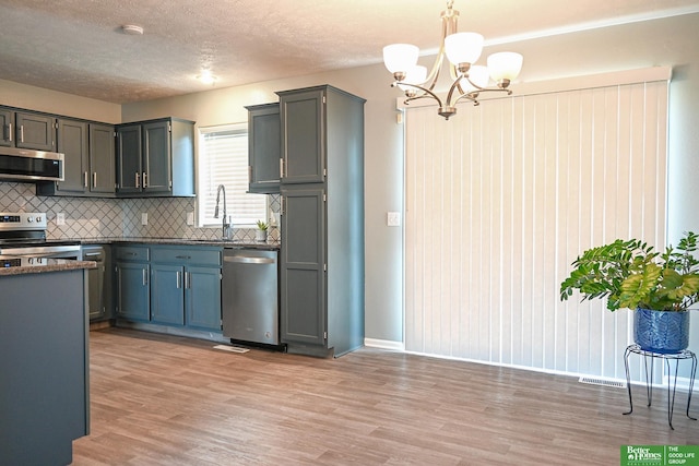 2412 Lewis And Clark Rd, Bellevue, NE 68123 - kitchen with appliances with stainless steel finishes, a chandelier, light wood finished floors, decorative backsplash, and pendant lighting