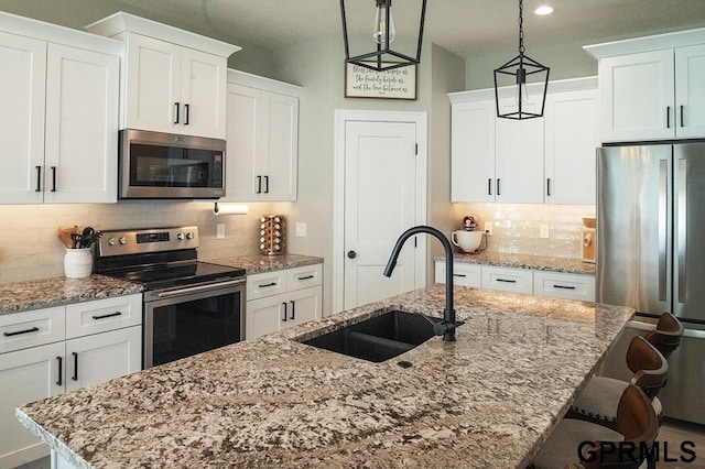 1600 W Avalanche Rd, Lincoln, NE 68521 - kitchen with appliances with stainless steel finishes, a kitchen island with sink, decorative backsplash, decorative light fixtures, and white cabinets
