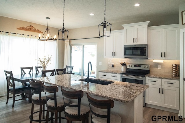1600 W Avalanche Rd, Lincoln, NE 68521 - kitchen with appliances with stainless steel finishes, a chandelier, tasteful backsplash, a kitchen island with sink, and white cabinetry