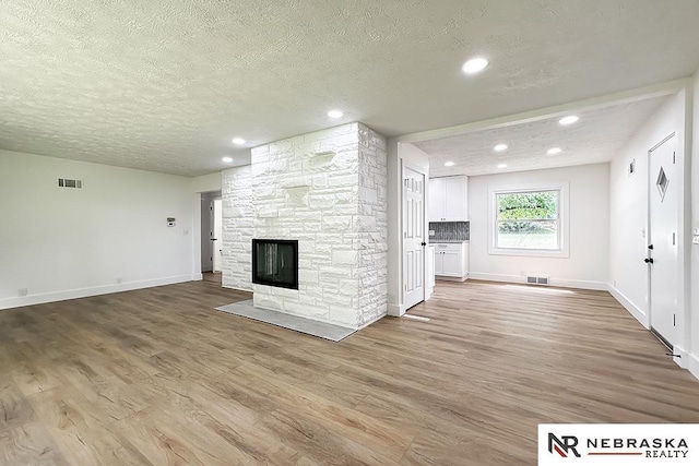 1113 S 94th St, Omaha, NE 68124 - unfurnished living room with a textured ceiling, light wood finished floors, a stone fireplace, and recessed lighting