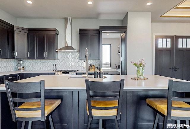 8150 S 185th St, Omaha, NE 68136 - kitchen featuring wall chimney range hood, decorative backsplash, light countertops, recessed lighting, and a center island with sink