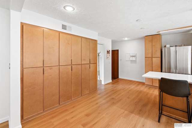 1133 S 96th St, Omaha, NE 68124 - kitchen with freestanding refrigerator, light wood-style floors, a kitchen bar, a textured ceiling, and recessed lighting
