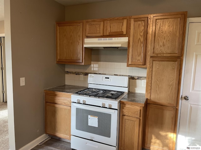 4317 Emmet St, Omaha, NE 68111 - kitchen featuring white range with gas cooktop, under cabinet range hood, dark countertops, decorative backsplash, and brown cabinetry
