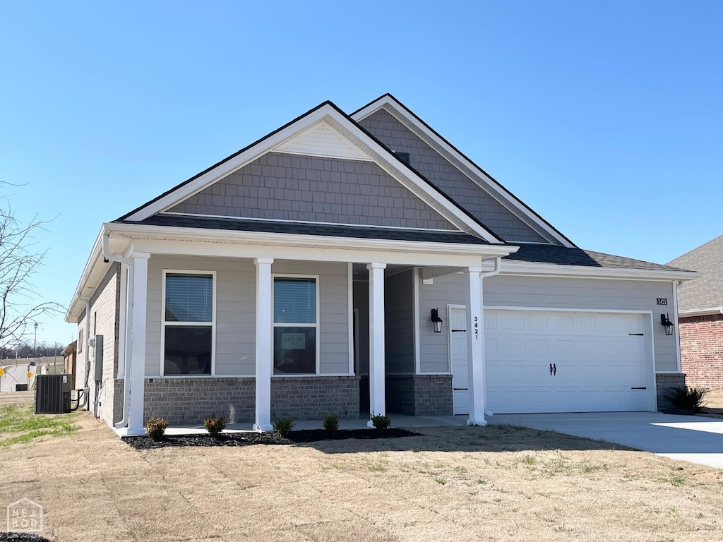 view of front of property featuring an attached garage, a porch, cooling unit, brick siding, and driveway