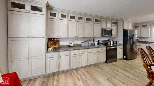 kitchen with dark countertops, appliances with stainless steel finishes, light wood-style floors, and a textured ceiling