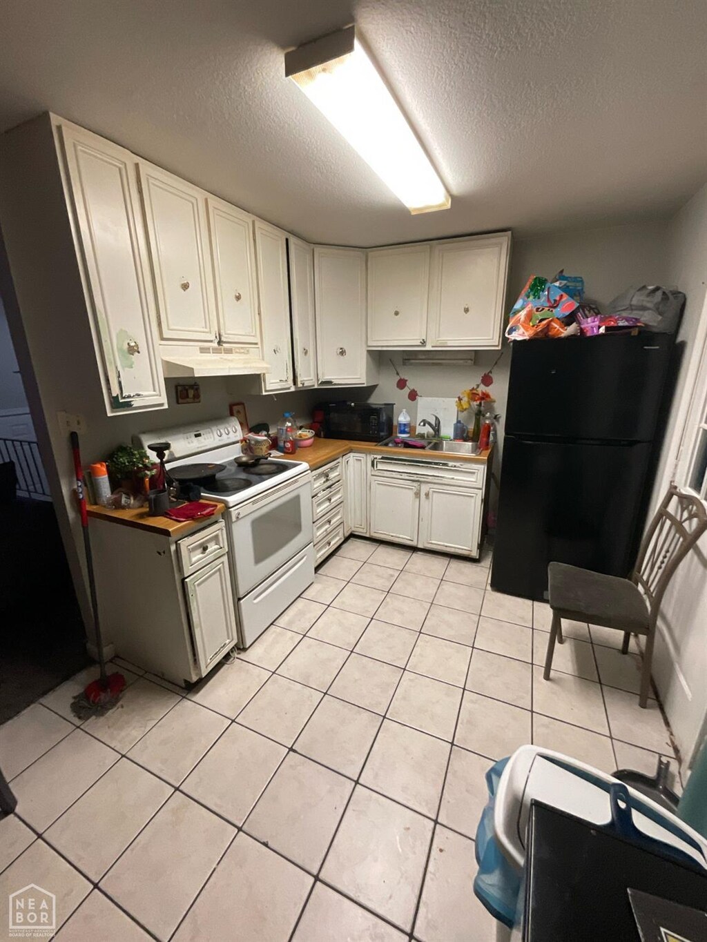 kitchen featuring a textured ceiling, white cabinetry, light tile patterned flooring, under cabinet range hood, and black appliances