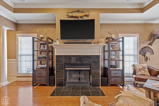 living area featuring decorative columns, a fireplace, ornamental molding, and wood finished floors