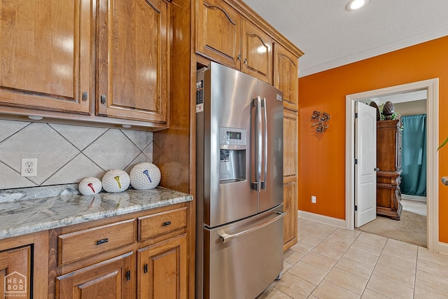 kitchen with stainless steel fridge with ice dispenser, light stone counters, light tile patterned flooring, brown cabinets, and decorative backsplash