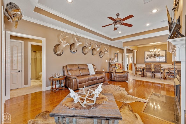 living room with ceiling fan with notable chandelier, wood finished floors, ornamental molding, and a raised ceiling