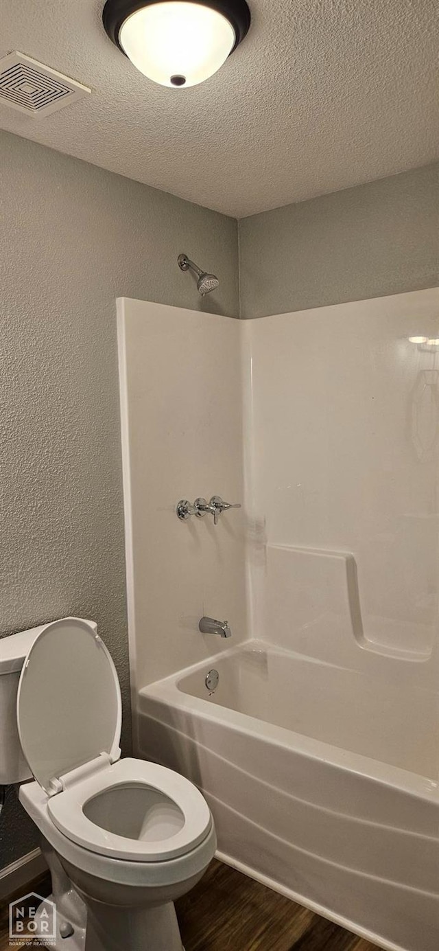 full bath featuring shower / washtub combination, a textured ceiling, visible vents, toilet, and wood finished floors