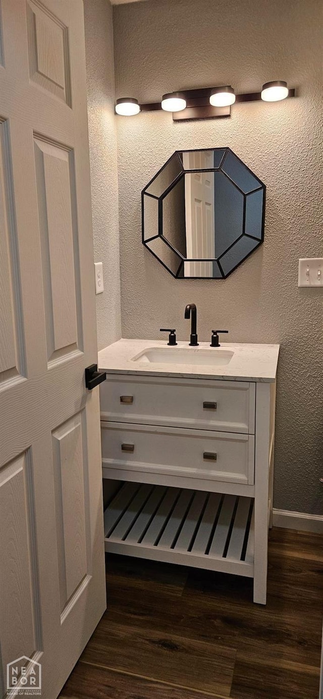 bathroom with wood finished floors, a textured wall, baseboards, and vanity