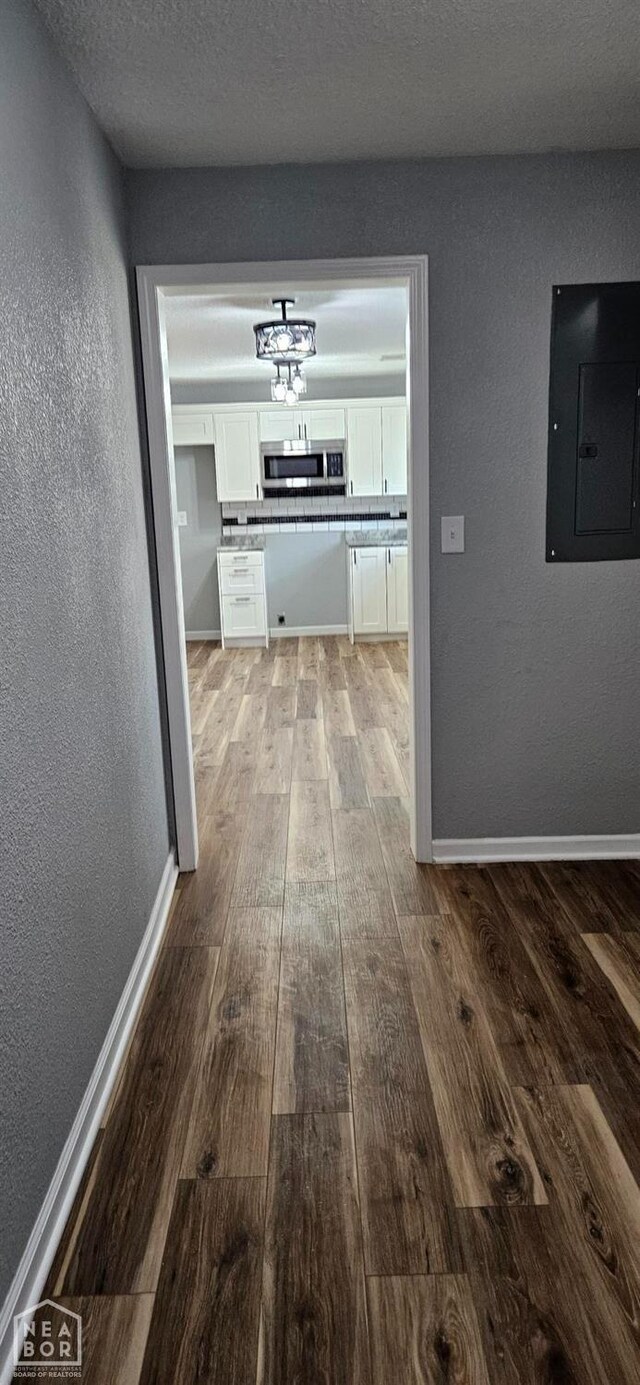hallway with electric panel, light wood-type flooring, baseboards, and a textured wall