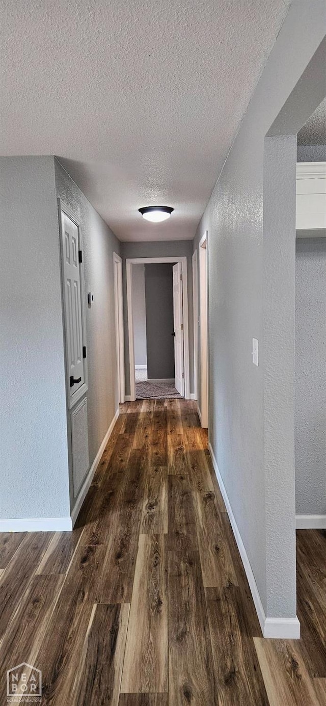 corridor featuring a textured wall, baseboards, wood finished floors, and a textured ceiling