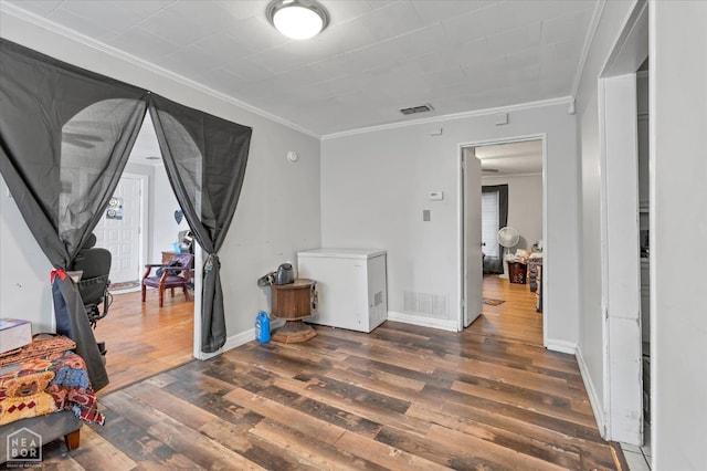 interior space with visible vents, wood finished floors, baseboards, and ornamental molding