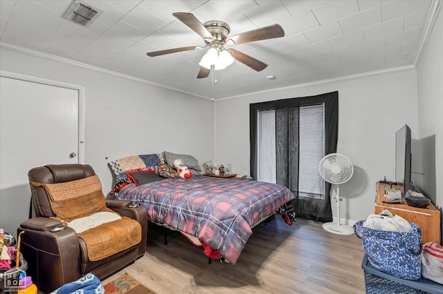 bedroom with crown molding, ceiling fan, visible vents, and wood finished floors