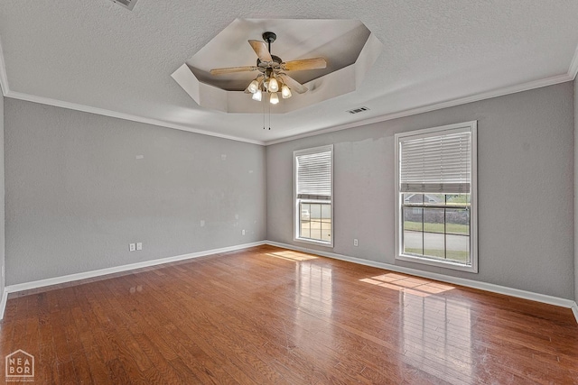 empty room with ornamental molding, visible vents, a tray ceiling, ceiling fan, and wood finished floors