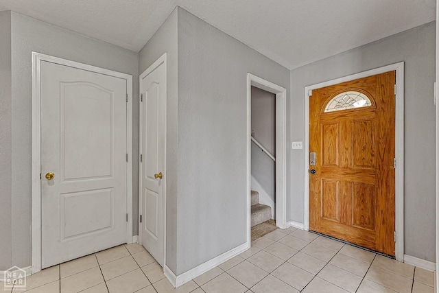 foyer featuring a textured ceiling, light tile patterned floors, baseboards, and stairs