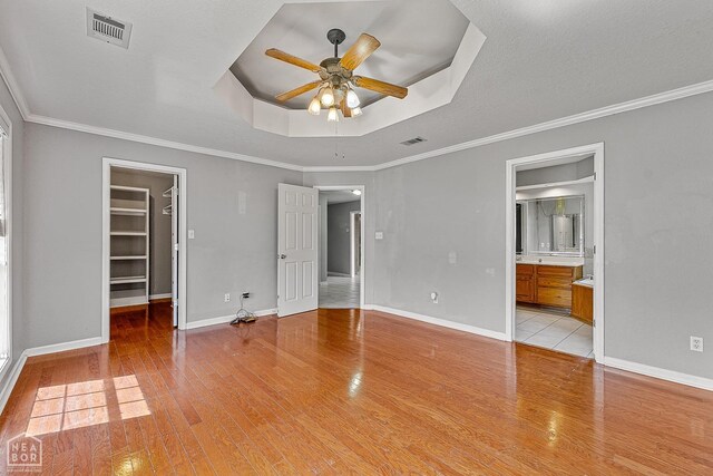 unfurnished bedroom featuring light wood-type flooring, baseboards, a walk in closet, visible vents, and a raised ceiling