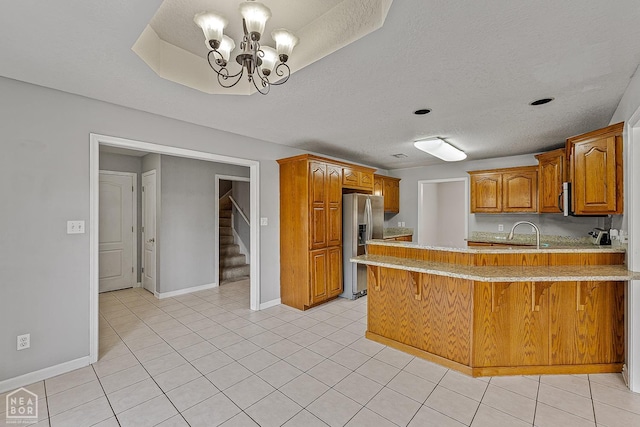 kitchen with stainless steel fridge, a chandelier, a peninsula, a textured ceiling, and brown cabinets