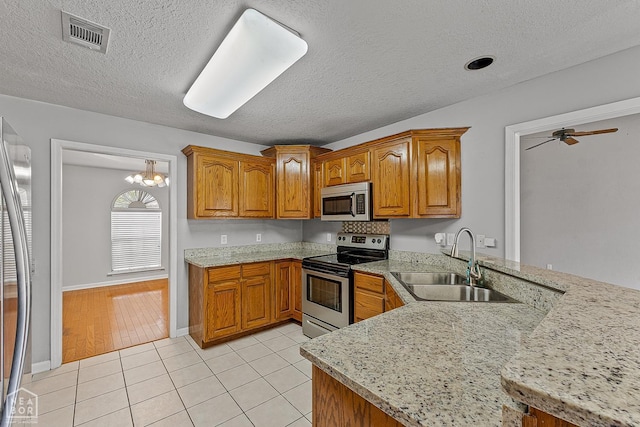 kitchen with visible vents, light tile patterned flooring, a sink, stainless steel appliances, and brown cabinets