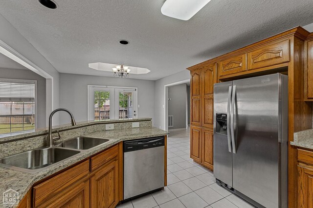 kitchen with light tile patterned floors, brown cabinetry, appliances with stainless steel finishes, a sink, and a notable chandelier