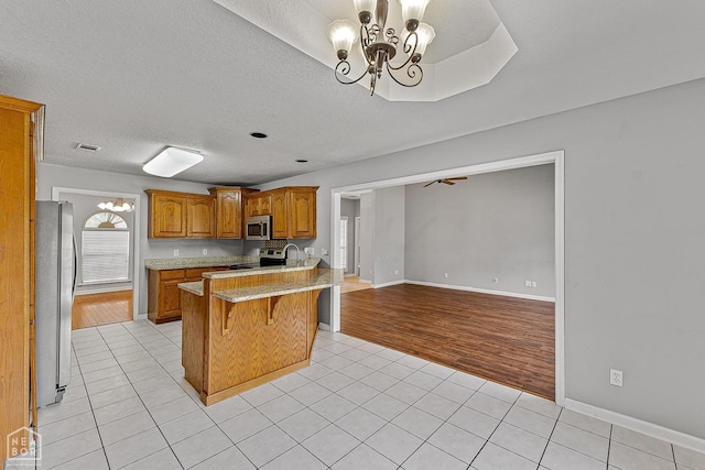 kitchen with a notable chandelier, light tile patterned flooring, a breakfast bar area, brown cabinetry, and stainless steel appliances