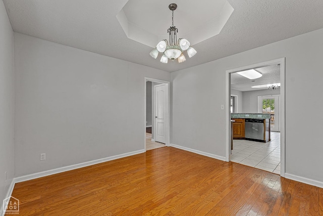 spare room with a raised ceiling, light wood-type flooring, a notable chandelier, and a textured ceiling