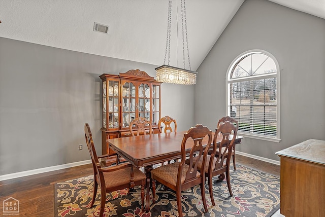dining space with an inviting chandelier, high vaulted ceiling, visible vents, wood finished floors, and baseboards