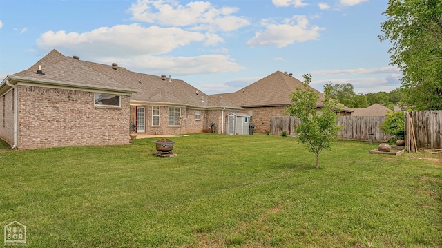 back of house featuring a shingled roof, brick siding, a storage unit, a fire pit, and fence