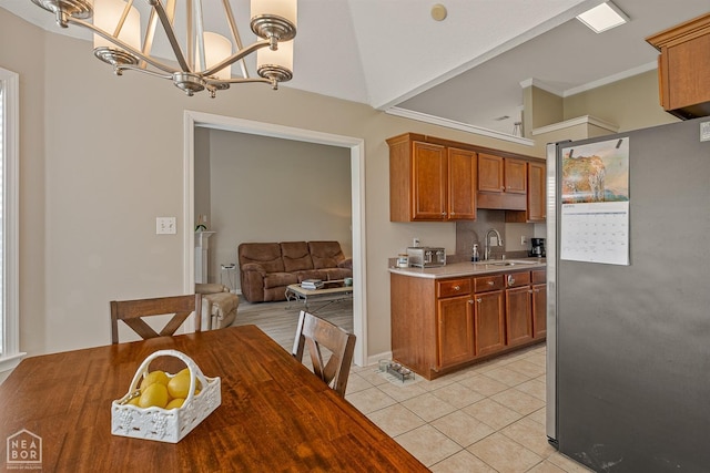 kitchen featuring light tile patterned floors, brown cabinets, a sink, freestanding refrigerator, and a notable chandelier