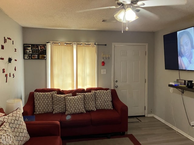 living room with a textured ceiling, a ceiling fan, visible vents, wood finished floors, and baseboards