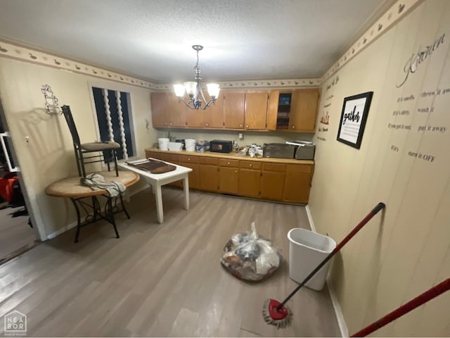 kitchen with light wood-style floors, light countertops, hanging light fixtures, brown cabinets, and a notable chandelier