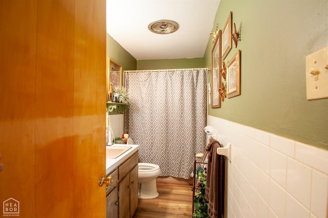 full bathroom featuring toilet, wood finished floors, a shower with shower curtain, vanity, and a wainscoted wall