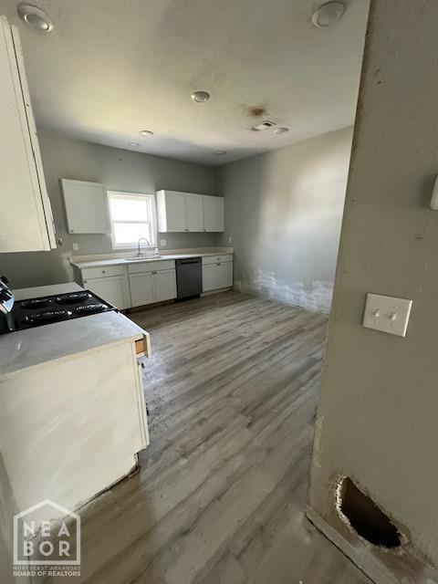 kitchen with light wood-style floors, white cabinetry, black appliances, light countertops, and a sink