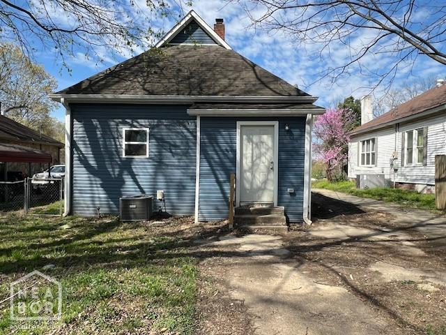 rear view of property featuring cooling unit, a lawn, entry steps, fence, and a chimney