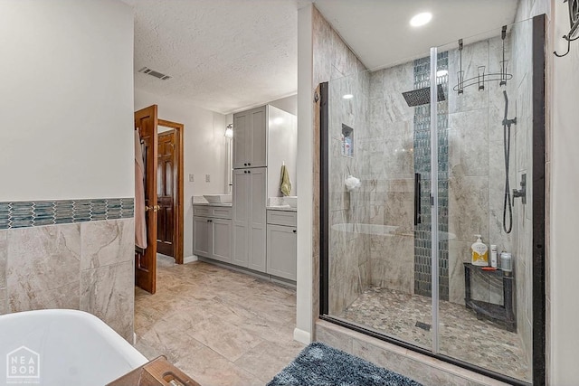 bathroom with tile walls, visible vents, a freestanding tub, a shower stall, and vanity