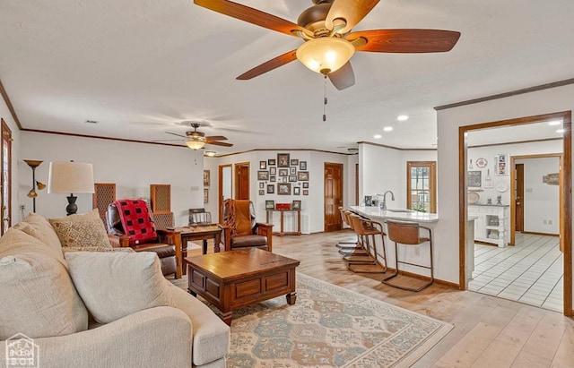 living area with light wood-style floors, ceiling fan, baseboards, and ornamental molding
