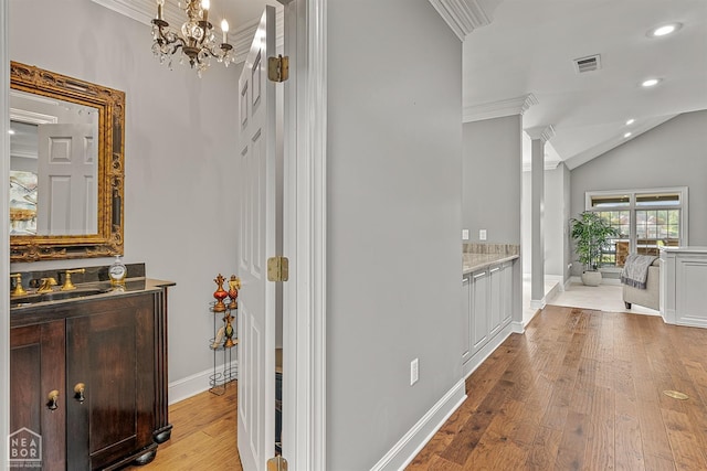 hall with a sink, ornamental molding, light wood-type flooring, baseboards, and a chandelier
