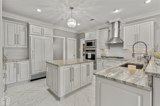 kitchen with wall chimney range hood, built in appliances, a sink, decorative light fixtures, and light stone counters
