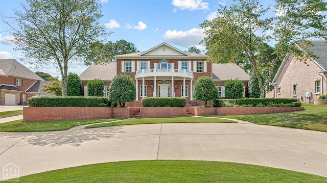 view of front facade with a balcony, brick siding, and a front yard